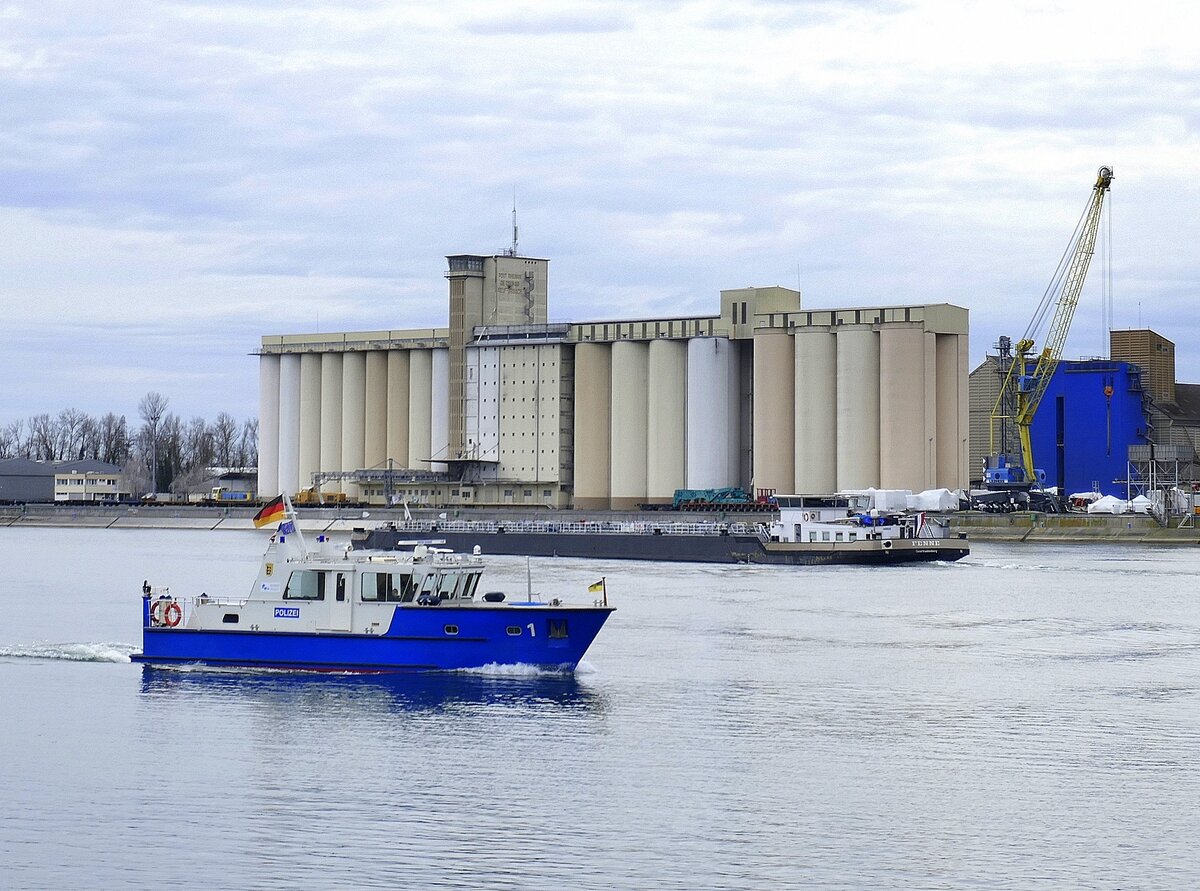 Polizeiboot und TMS Fenne begegnen sich auf dem Rhein, im Hintergrund der Hafen Neubreisach (Neuf-Brisch) im Elsaß, Feb.2025